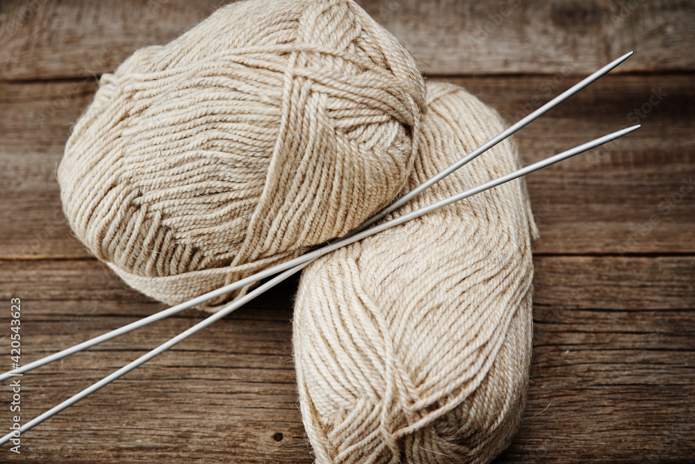 Two skeins of woolen yarn and needles for knitting on a wooden background