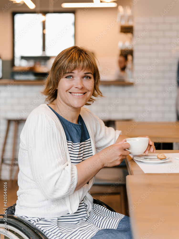 Happy woman using wheelchair having cup of coffee in cafeteria Happy woman using wheelchair having cup of coffee in cafeteria