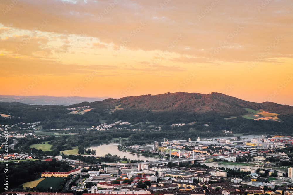 sunset falls on city of Linz in northern Austria. Beautiful orange sky and the eastern part of city. Linzertorte is immersed in red-orange light and sky is reflected from the Danube River