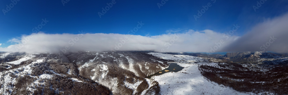 Obraz premium Drone shooting at 180 degrees of the Biviere lake in the heart of the Nebrodi mountains in winter. View of Etna and the Aeolian Islands. Sicily in winter. Sicilian mountains.