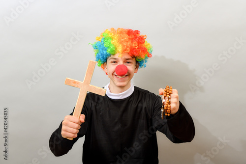 A clown dressed as a Catholic pastor with a cross and a rosary. The concept of blasphemy and ridicule of religion. photo