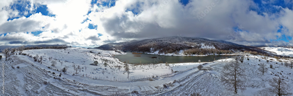Obraz premium Drone shooting at 180 degrees of the Biviere lake in the heart of the Nebrodi mountains in winter. View of Etna and the Aeolian Islands. Sicily in winter. Sicilian mountains.