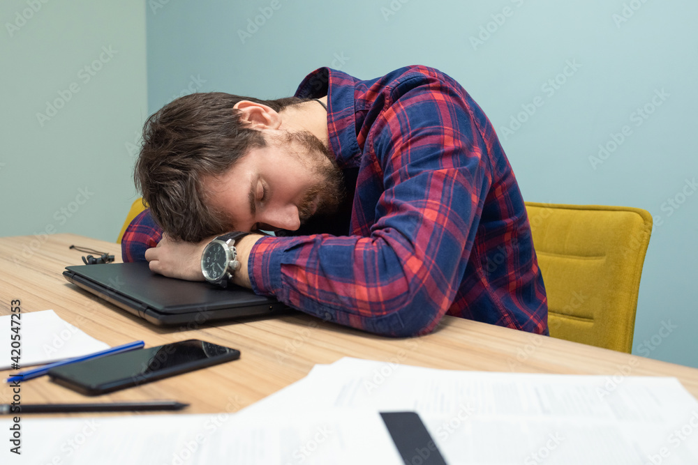 Young tired businessman sleeping at his desk in the office. Overwork, side view Young tired businessman sleeping at his desk in the office. Overwork, side view