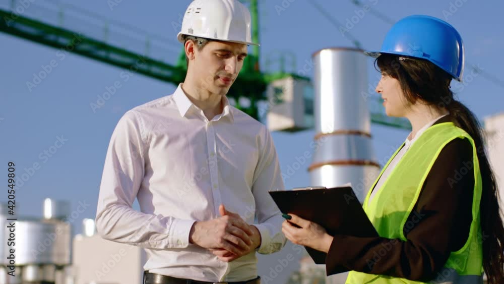 On construction site good looking lady architect and engineer man have a discussing on the construction site they analyzing the next steps of plan at the end they shanking hands and wearing safety On construction site good looking lady architect and engineer man have a discussing on the construction site they analyzing the next steps of plan at the end they shanking hands and wearing safety
