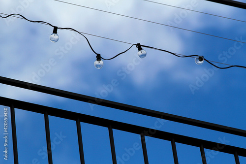 Billede på lærred String of unlit light bulbs silhouetted against the blue sky.