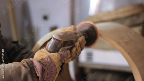 close-up of grinding solid wood with a round emery nozzle on an electric drill in the hands of a carpenter, part of the workflow for finishing a fragment of a wooden product in a carpenter's workshop