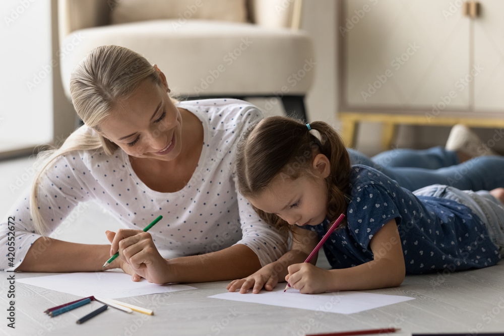Loving happy young Caucasian mom and little daughter lying on floor drawing in album together. Caring smiling mother and small girl child have fun relax paining, involved in artistic activity. Loving happy young Caucasian mom and little daughter lying on floor drawing in album together. Caring smiling mother and small girl child have fun relax paining, involved in artistic activity.