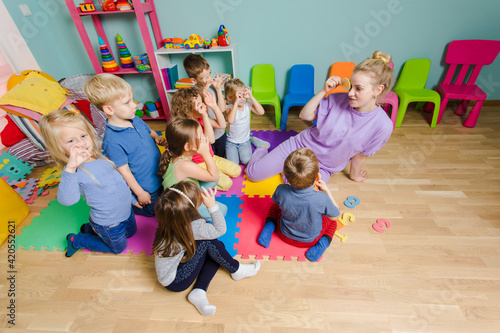 Preschool teacher teaching group of children, sitting on a floor