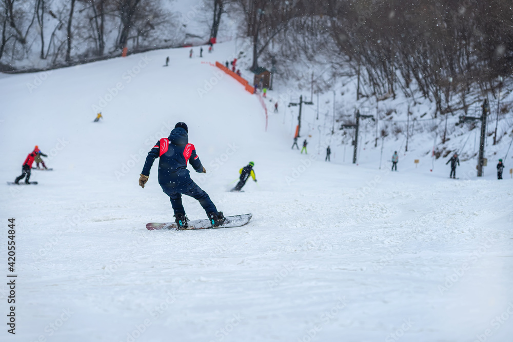 Down slope on snow covered mountain. Back view of snowboarder riding on slope, blurred selective focus
