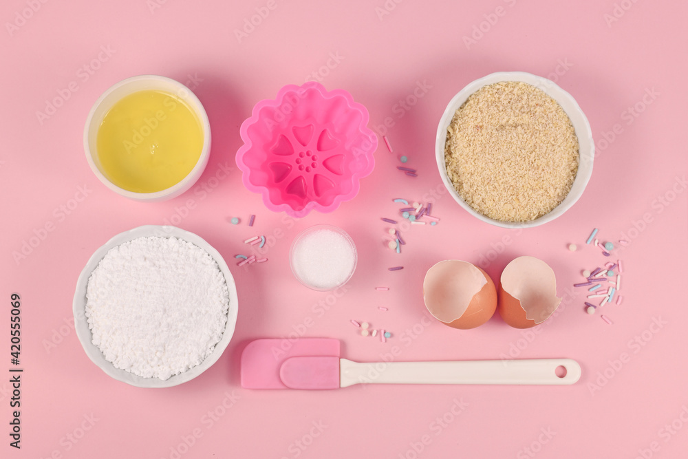 Baking ingredients and tools like powdered sugar, ground almonds, egg white, salt, sugar sprinkles and cake mold on pink background Baking ingredients and tools like powdered sugar, ground almonds, egg white, salt, sugar sprinkles and cake mold on pink background
