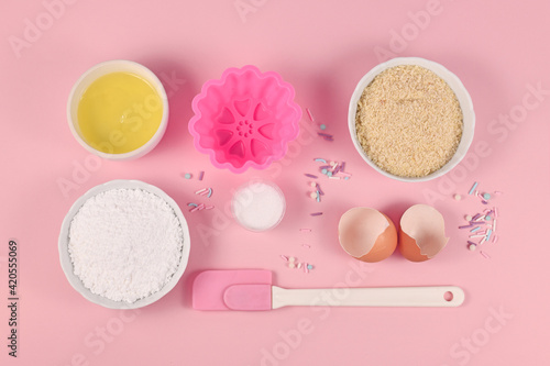 Baking ingredients and tools like powdered sugar, ground almonds, egg white, salt, sugar sprinkles and cake mold on pink background