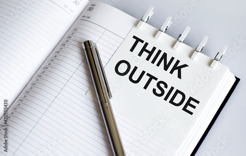 text Think Outside on the short note texture background with pen