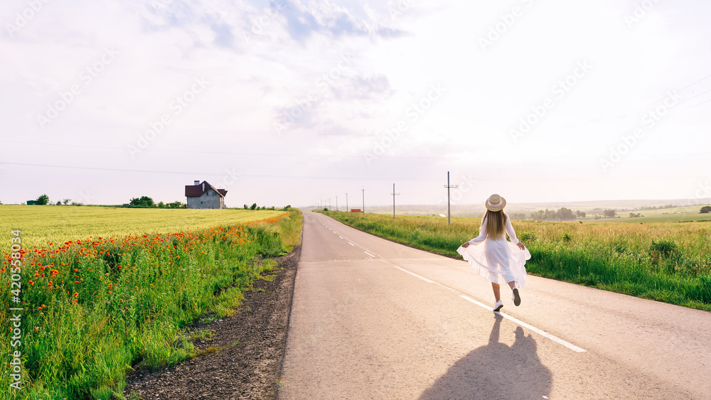 back view of girl in dress and boater walks on the road near the