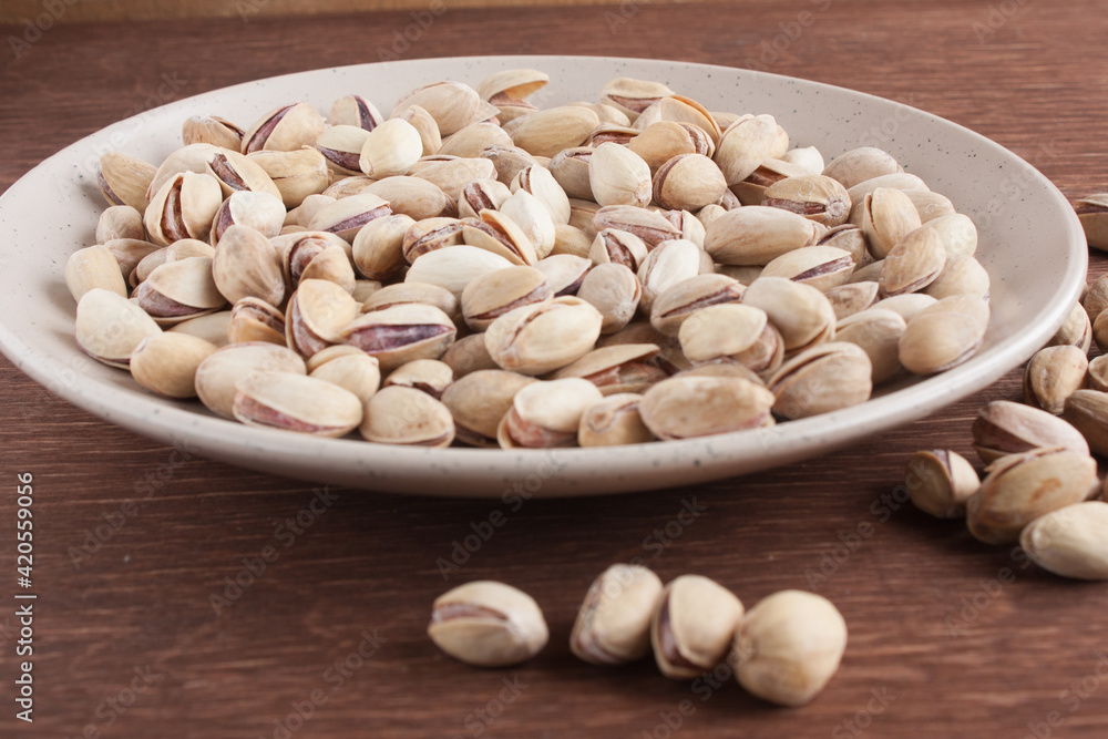 Fried salted pistachios in a light plate on a wooden table Fried salted pistachios in a light plate on a wooden table