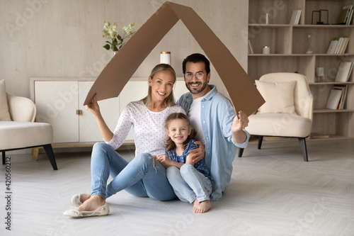 Portrait of happy young Caucasian family with daughter relax under roof celebrate relocation to own home. Smiling parents with girl child enjoy new house or apartment. Rental, real estate concept.