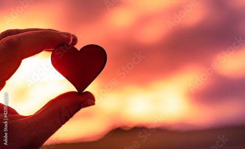 Hand holding heart on sunset background. Love symbol 