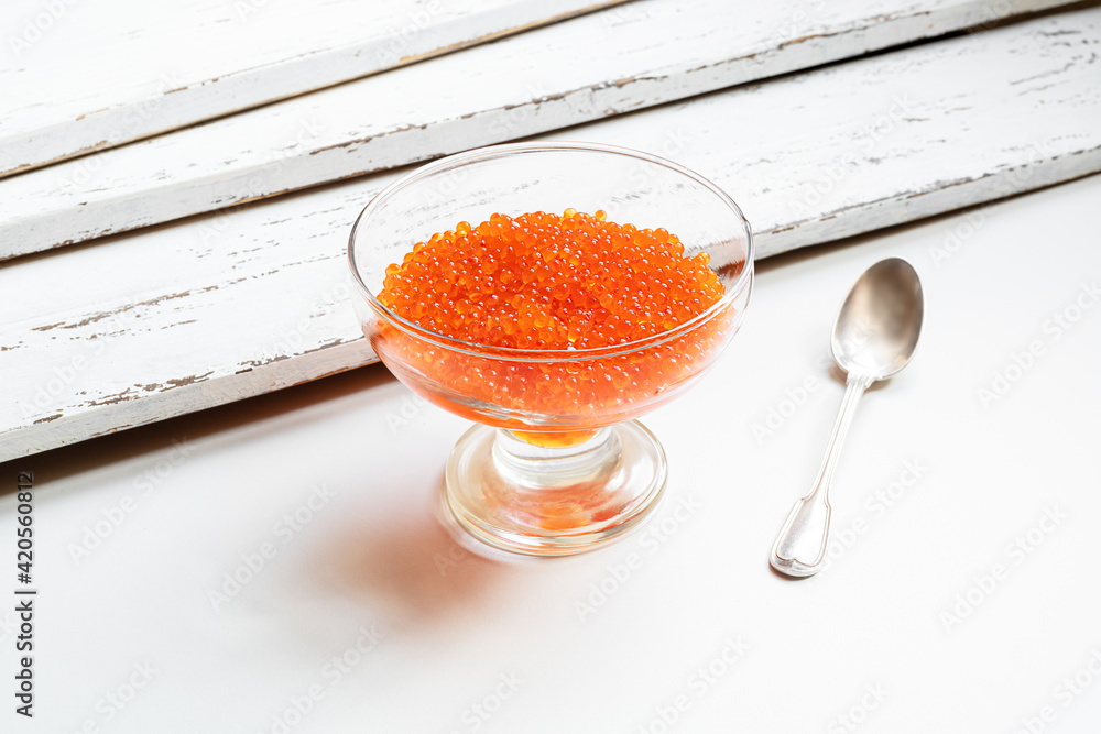 Red salmon caviar in a transparent glass and a silver spoon on a white table Red salmon caviar in a transparent glass and a silver spoon on a white table