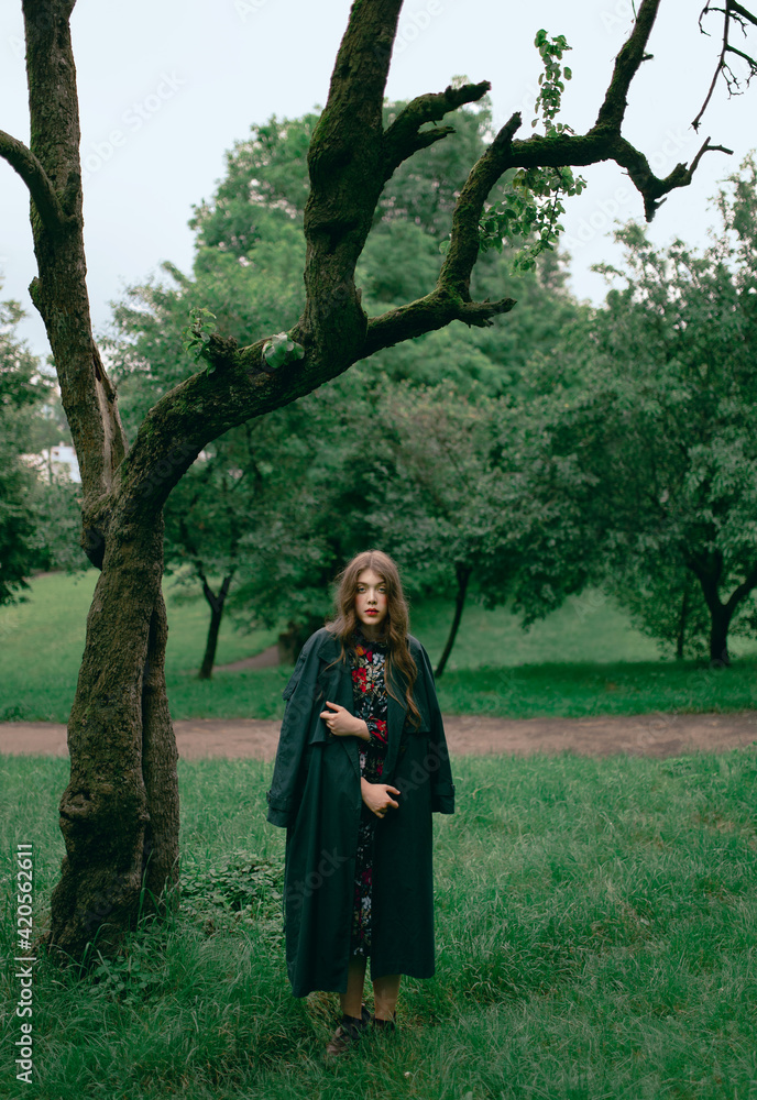 Young woman with trench coat standing hext to a tree Young woman with trench coat standing hext to a tree