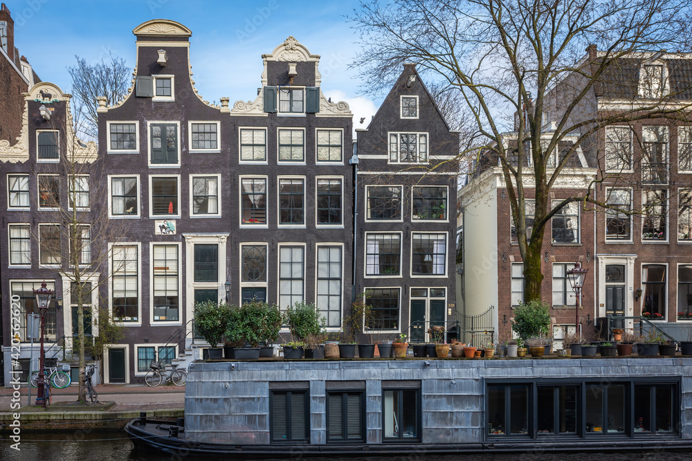 Fototapeta premium A view of the houseboat and a typical dutch houses along the Prinsengracht canal in Amsterdam