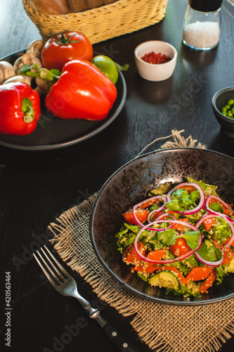 Quinoa salad with tomatoes, avocado, paprika and parsley on black stone plate.