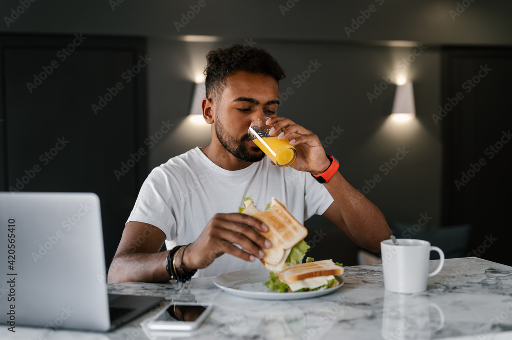 Ethnic man eating sandwiches and watching video on laptop Ethnic man eating sandwiches and watching video on laptop