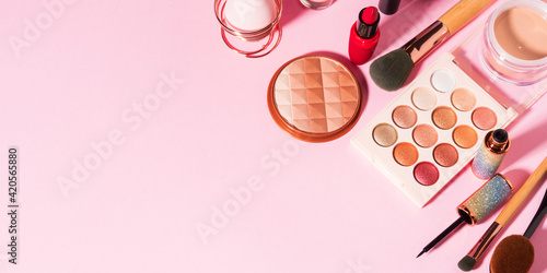 Different make up beauty cosmetics products on pink pastel background. Foundation, lipstick, eye shadows, brushes, face powder, eyeliner