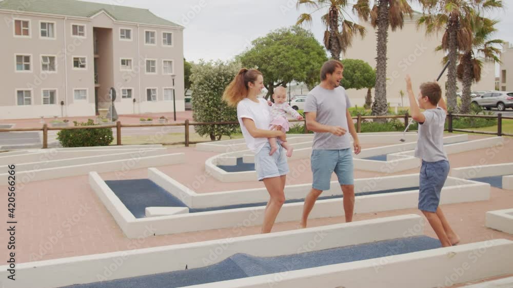 Family of four playing on miniature golf course, boy making putt into hole. Family of four playing on miniature golf course, boy making putt into hole.