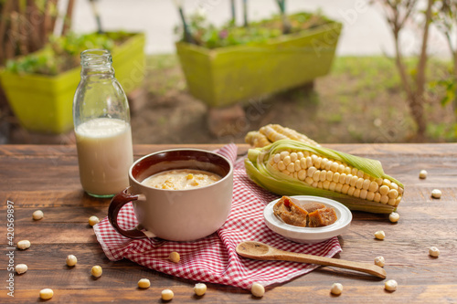 Mazamorra cup with panela pieces, milk bottle and cobs over rustic wood table in natural background photo