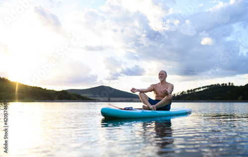 Senior man on paddleboard on lake in summer, doing yoga exercise. © Halfpoint