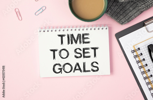 TIME TO SET GOALS written in a white notebook on a pink background near the pen