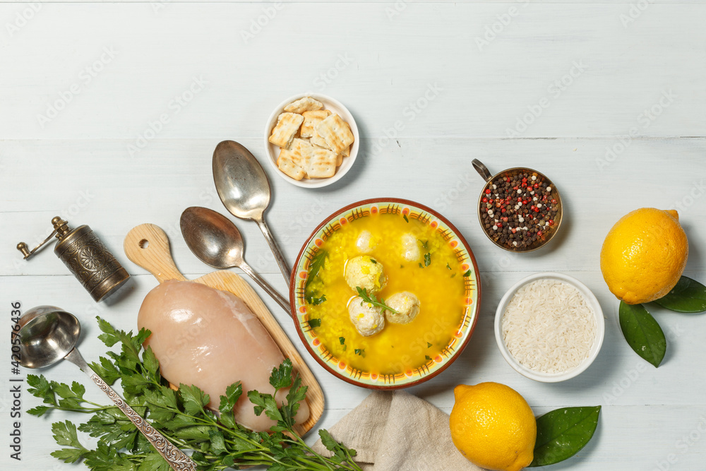 Avgolemono, Greek traditional soup, in a ceramic painted bowl. On a gray wooden table with cooking supplies, spoons, and a pepper mill. Avgolemono, Greek traditional soup, in a ceramic painted bowl. On a gray wooden table with cooking supplies, spoons, and a pepper mill.