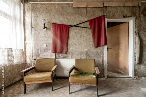 Room with 2 chairs and 2 red flags on the wall in run-down hotel, front view