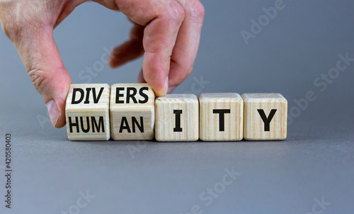 Diversity and humanity symbol. Businessman turns wooden cubes and changes the word 'humanity' to 'diversity'. Beautiful grey background. Business, diversity and humanity concept. Copy space.