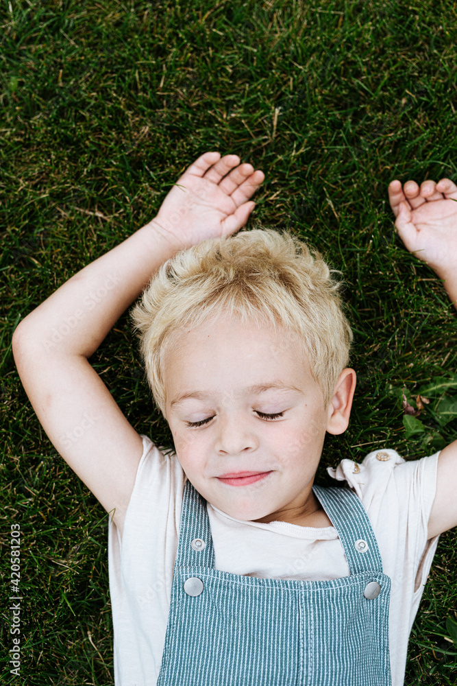 sweet blond toddler boy lying on the grass outdoors sweet blond toddler boy lying on the grass outdoors