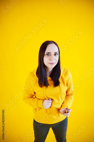 Portrait of young woman on yellow background. Pretty brunette in yellow hoodie posing on bright background. © Anton Dios