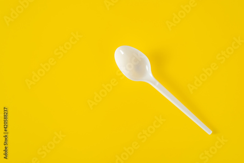 Plastic spoon on yellow background. Picnic plastic disposable tableware, copy space