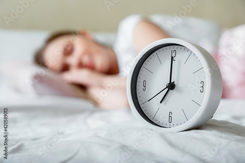 Happy young woman sleeping near bed side alarm clock. Calm healthy morning sleep of woman in pajamas. Morning routine and wake up from alarm clock.