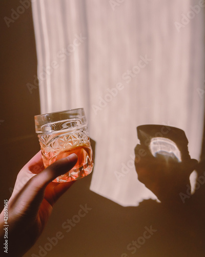 female hand holding glass cocktail sunlight shadow