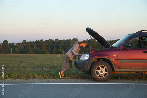 Woman examining engine of broken car in countryside