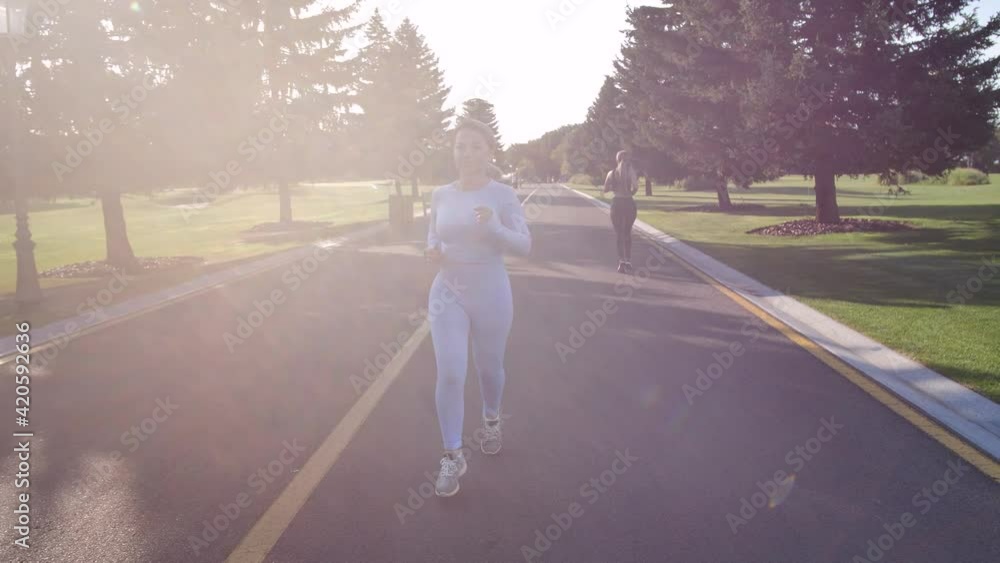Pretty female jogger in tight blue sportswear running along park alley in bright sunlight. Fit woman during cardio training at nature. Healthy sports lifestyle, outdoors leisure activity concept Pretty female jogger in tight blue sportswear running along park alley in bright sunlight. Fit woman during cardio training at nature. Healthy sports lifestyle, outdoors leisure activity concept