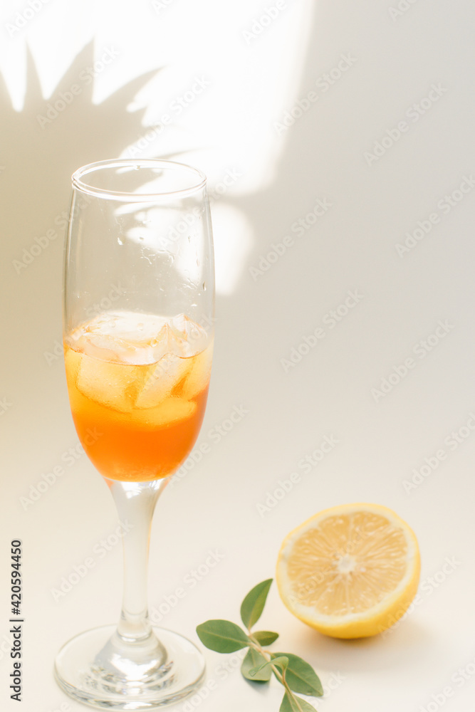Cold refreshing drink with lemon orange slices by the glass on white background on directly sunlight with shadows Cold refreshing drink with lemon orange slices by the glass on white background on directly sunlight with shadows