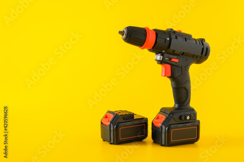 Modern black cordless screwdriver, drill with recharge battery on yellow background, copy space for text
