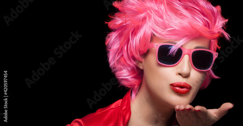 Stylish sensual woman with trendy modern sunglasses and pink short hair blowing across the palm of her hand sending a kiss with pouting red lips