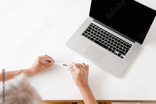 Unrecognizable senior woman with thermometer near laptop photo