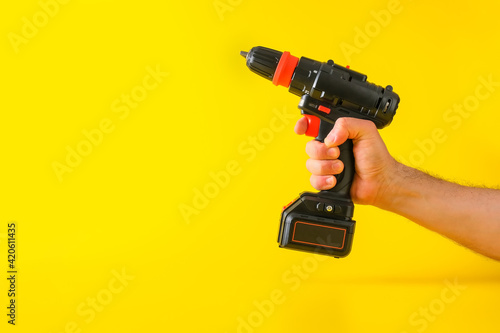 Cordless battery powered screwdriver on yellow background with cropped male hand holding tool for repair or building construction, copy space for text