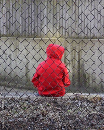 Boy in Red Alone and Sad Behind Fence photo