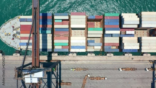 Vertical mobile video 9:16. Aerial top down view on unloading of cargo ship in port dock. Heavy shipping metal containers being loaded by industrial cranes. Water transportation, delivery business 4K