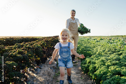 Female farmer with child harvesting greens in field photo