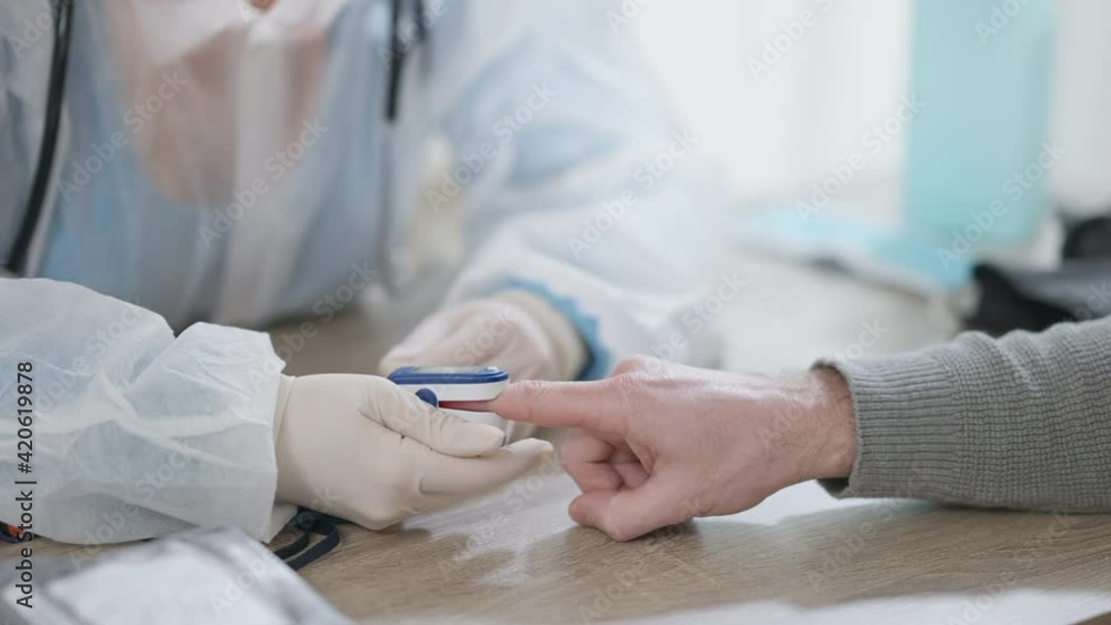 Unrecognizable doctor or nurse in gloves measuring oxygen saturation and pulse rate of patient with pulse oximeter. Professional woman pressing device on man fingertip. Health care concept. Unrecognizable doctor or nurse in gloves measuring oxygen saturation and pulse rate of patient with pulse oximeter. Professional woman pressing device on man fingertip. Health care concept.