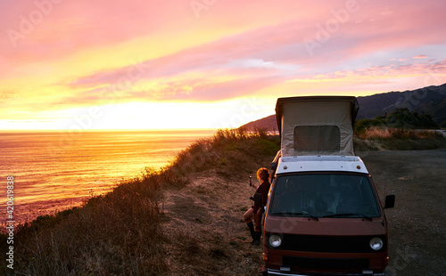 Wanderlust woman recording a beautiful sunset over the west coast of california during a roadtrip with her vintage campervan photo